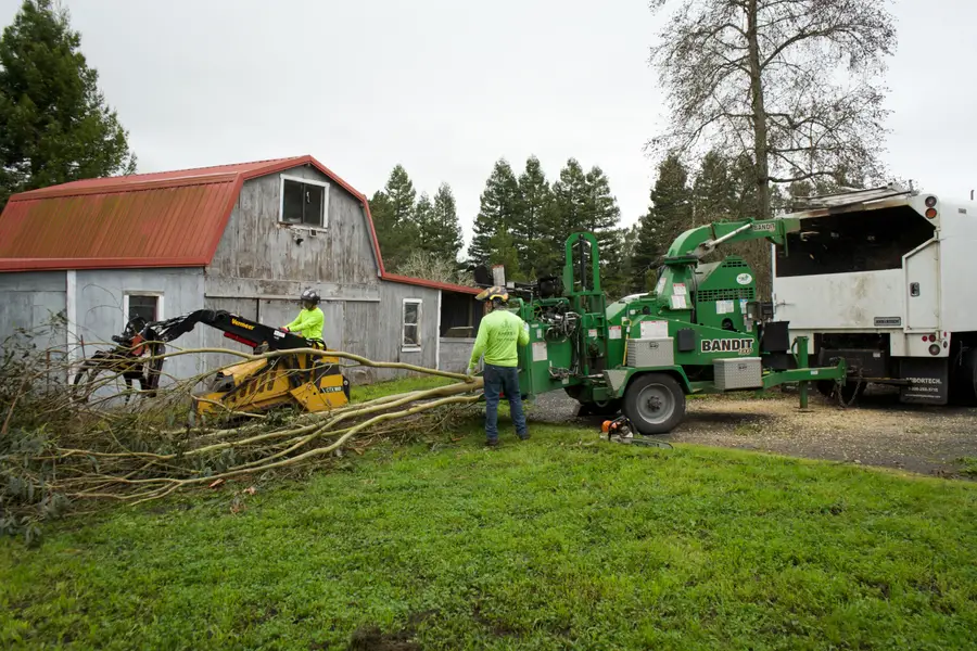 Track loader and Bandit chipper working beside a barn